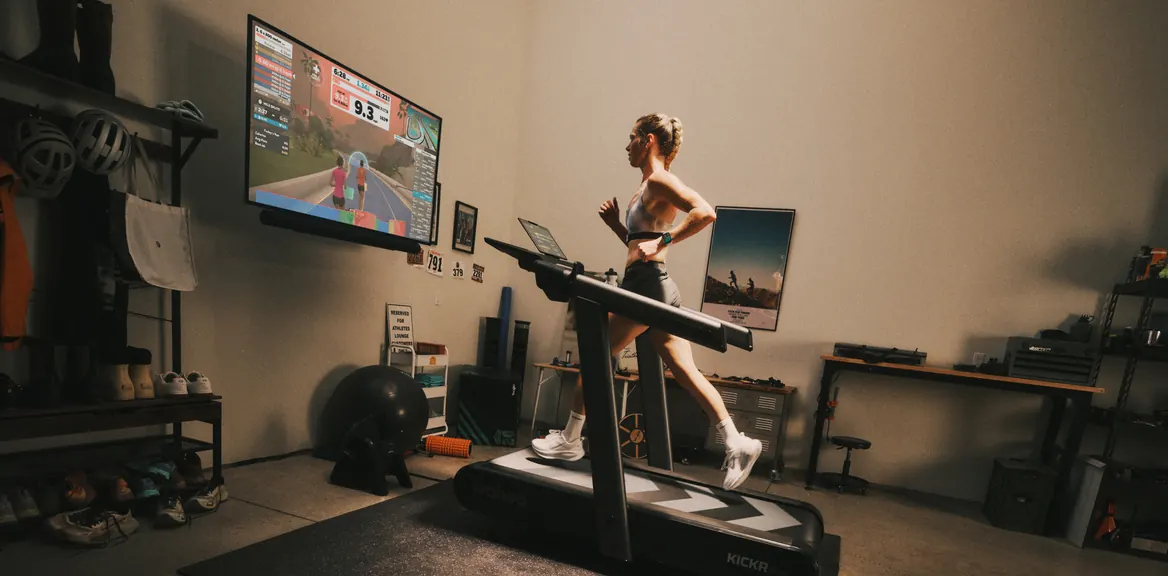 A runner mid-stride on a Wahoo KICKR RUN treadmill in a garage gym, a virtual route on the screen ahead